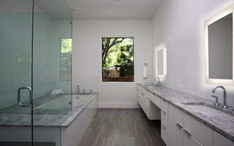 A grey marble vanity and tub surround with a glass shower and double sinks with sleek white cabinets bathroom design in Austin, Texas.